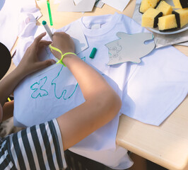A child uses a stencil to draw a pattern on a T-shirt