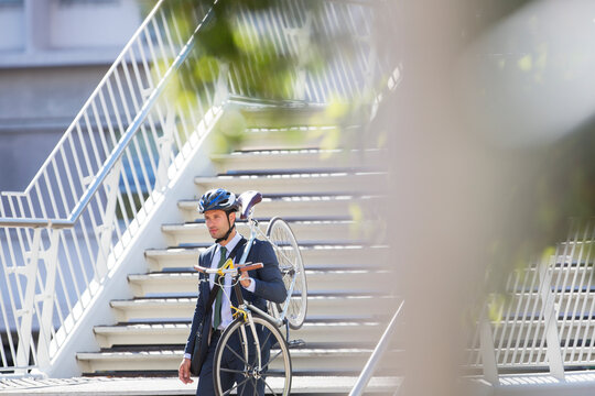 Businessman in suit and helmet carrying bicycle down urban stairs - Powered by Adobe