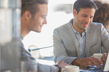 Businessmen with coffee working at laptop in cafe