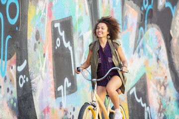Smiling brunette woman riding bicycle along urban multicolor graffiti wall