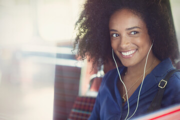 Smiling woman with afro listening to music with headphones on bus - obrazy, fototapety, plakaty