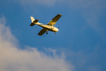 One-engine plane flying in blue sky over clouds