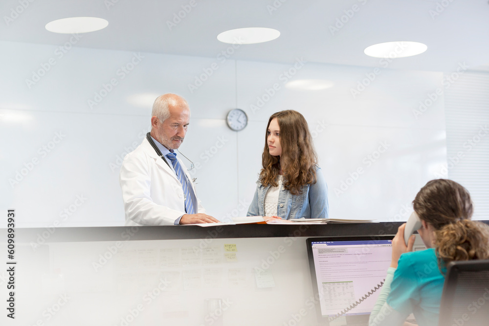 Wall mural Doctor and teenage patient discussing medical record at nurses station - Wall murals