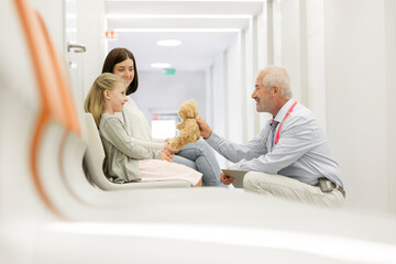 Doctor with teddy bear talking to girl patient in clinic corridor