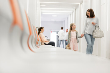 Mother and daughter holding hands walking in hospital corridor