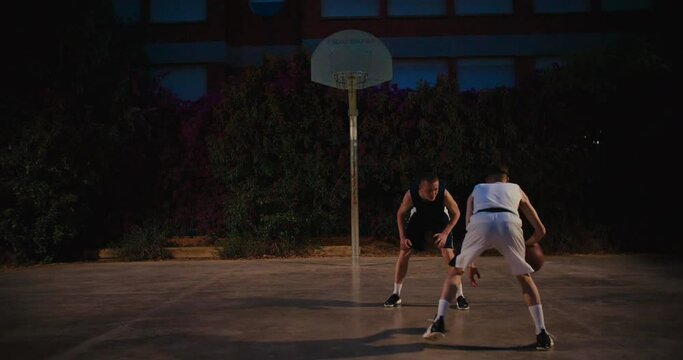 Night Time Practice After Work, Street Basketball Training. Two Friends Play Match On Outdoor Court In Park. Athletic Active Youth. Urban City Life. Sports In City Environment