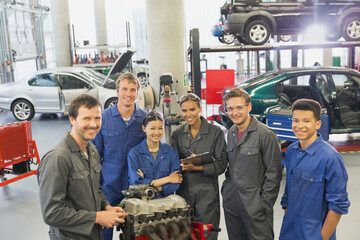 Portrait confident mechanics with car engine in auto repair shop