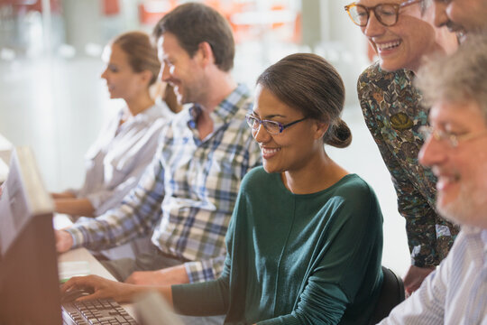 Smiling adult education students working together at computer in classroom