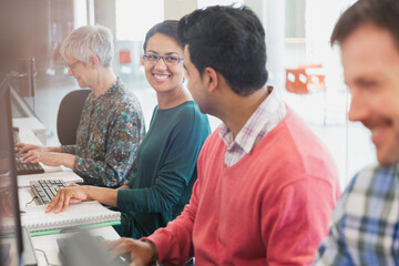 Fototapeta premium Smiling students talking at computers in adult education classroom