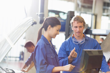 Mechanics discussing part at computer in auto repair shop