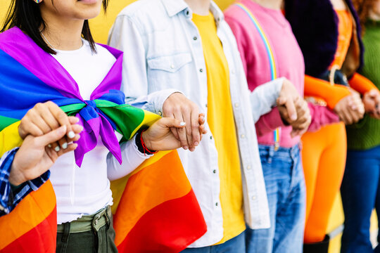 Young group of LGBT community people holding hands outdoors showing support, equality, inclusion and unity. Young activist demonstrator celebrating gay pride day festival in city street. - Powered by Adobe