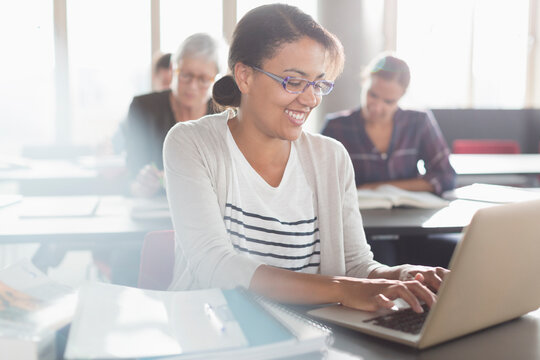 Smiling woman typing at laptop in adult education classroom
