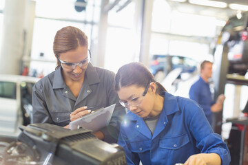 Female mechanics working on engine in auto repair shop