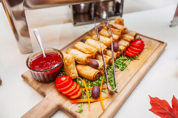 Wooden board of delicious spring rolls, tomato sauce, fresh salad and nutritious ingredients. Catering service, event in restaurant.