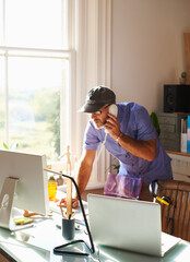 Man talking on telephone using computer at desk in sunny home office