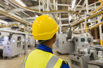 Worker in hard-hat watching printing press conveyor belts machinery in printing plant