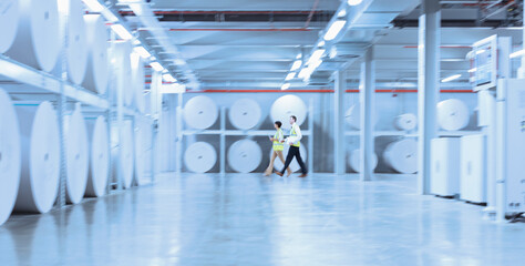 Workers walking along large paper spools in printing plant