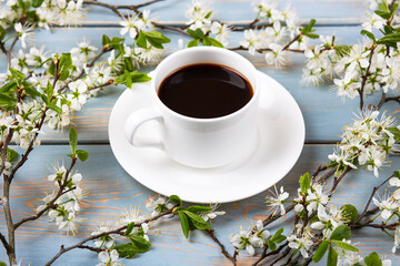Cup of fresh black coffee and cherry blossom branches on blue wooden background. Coffee break. Spring flowers.