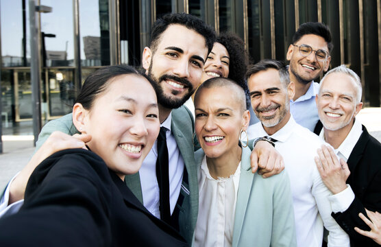 Multiracial group of cheerful and successful business people taking a selfie outside. Diverse office colleagues laughing taking a picture together smiling and bonding in the street.