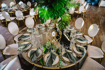 Round served banquet tables ready for guests, decorated plate, glasses, forks, emerald green...