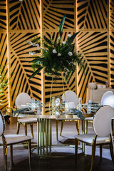 Banquet decoration composition flower greenery in hall restaurant. Luxury wedding reception. Table setting, setup. Trendy decor for birthday party. Golden geometric chairs. Round served table guests.