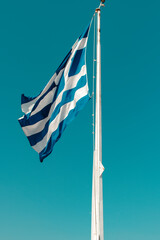 Greek flag on a flag pole with a blue sky background