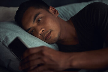 Dark, browse and man in bed with phone surfing internet, social media post or texting with insomnia...