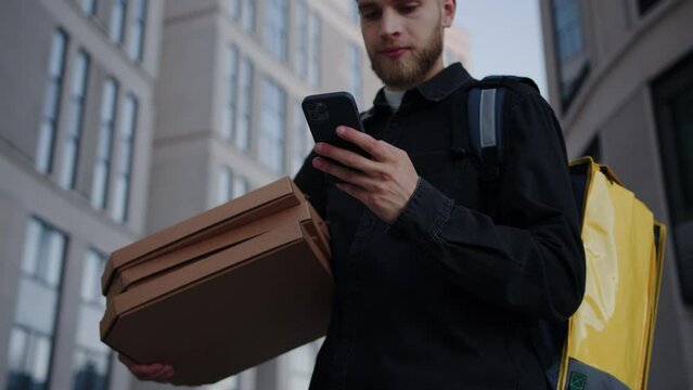The male courier is looking at the delivery address on the map in the phone outside