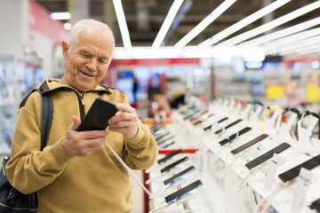 elderly grayhaired man pensioner examining counter with electronic gadgets and tablets in showroom...