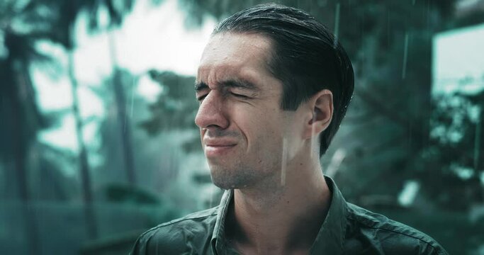 Cinematic portrait of an unhappy depressed male 30 suffering from mental problems while standing outside in the rain. Depressed man getting wet in the rain outdoors and having an emotional breakdown