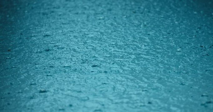 Close up heavy rain concept. Raindrops splashing blue puddle water surface, abstract natural background of a rainy day with heavy rains. Summer rain in Wet Season.