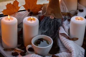 Thanksgiving and Hello Fall Halloween concept Celebrating autumn holidays at cozy home on the windowsill Hygge aesthetic atmosphere Autumn leaves gnome, spices and candle on knitted white sweater in