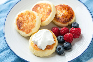 Syrniki, cottage cheese fritters served with fresh berries and sour cream on a plate. Russian, Ukrainian cuisine food for a healthy breakfast. Closeup view
