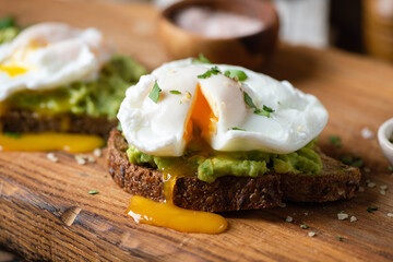 Poached egg on avocado toast served on a wooden board. Healthy breakfast or snack, closeup view