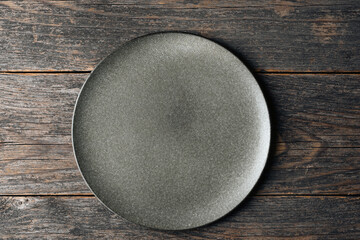 Empty craft ceramic plate on dark wooden table background. Top view. Design template, food...