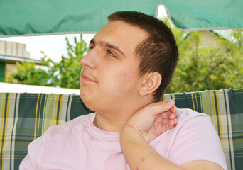 An autistic teenager rests on a walk, holding his hand near his face.