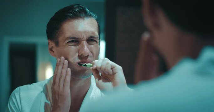 Reflection in the mirror, close up man brushing teeth in bathroom and feel dental pain discomfort suffer from toothache. Caries problem with teeth oral disease unwell illnesses. Dental problems