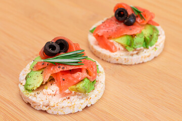 Rice Cake Sandwiches with Fresh Salmon, Avocado and Olives on Bamboo Cutting Board. Easy Breakfast. Diet Food. Quick and Healthy Sandwiches. Crispbread with Tasty Filling. Healthy Dietary Snack