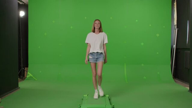 Woman in white t-shirt, jeans shorts and sneakers walking on a Green Screen, Chroma Key. 4k UHD front view footage video
