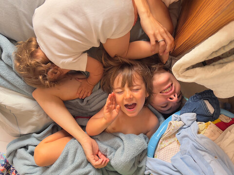 Overhead view of a mother and her children having fun on the floor among the clothes.