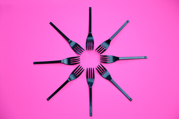 Top view composition of black plastic forks placed on pink background