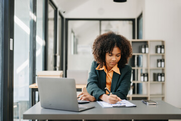 Confident business expert attractive smiling young woman typing laptop ang holding digital tablet on desk in office.