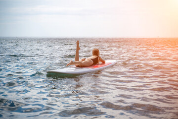 Woman sup sea. Sports girl on a surfboard in the sea on a sunny summer day. In a black bathing suit, he sits on a sapa in the sea. Rest on the sea.