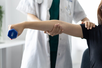 Doctor doing arm physiotherapy training for female patient in hospital.