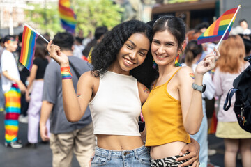 Couple beautiful woman holding rainbow flag at city street. They looking to camera with attractive smiling.