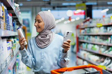 A young beautiful Muslim woman in a hijab chooses a product for washing hair, a shampoo, a...