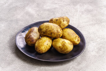 Raw potatoes on plate on concrete background