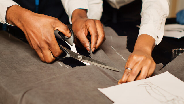 Team of tailors cutting material, preparing fabric for custom made clothing line in luxury workshop. Craftsman and assistant using scissors to cut for handcraft process. Handheld shot. Close up.