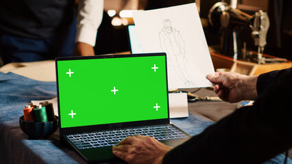 Craftsman using greenscreen on laptop, experienced tailor looking at chroma key display in workshop. Couturier designing items with isolated mockup template in tailoring atelier.
