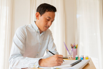 Man asian sitting and painting watercolour artwork to develop abilities and improve mental health at home. Female artist drawing with inspiration.